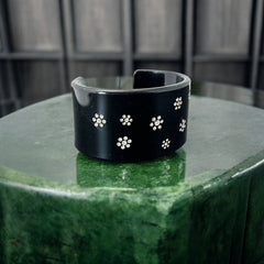 A vintage black plastic cuff bracelet featuring a sleek design with clear rhinestones arranged in small floral patterns. The bracelet, likely from the 2000s, is shown in very good condition with minimal surface scratching, adding timeless elegance and eco-conscious charm to any outfit.
