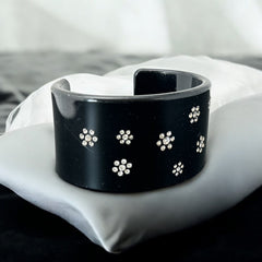 A vintage black plastic cuff bracelet featuring a sleek design with clear rhinestones arranged in small floral patterns. The bracelet, likely from the 2000s, is shown in very good condition with minimal surface scratching, adding timeless elegance and eco-conscious charm to any outfit.