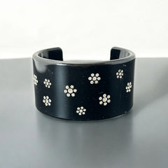 A vintage black plastic cuff bracelet featuring a sleek design with clear rhinestones arranged in small floral patterns. The bracelet, likely from the 2000s, is shown in very good condition with minimal surface scratching, adding timeless elegance and eco-conscious charm to any outfit.