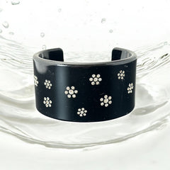 A vintage black plastic cuff bracelet featuring a sleek design with clear rhinestones arranged in small floral patterns. The bracelet, likely from the 2000s, is shown in very good condition with minimal surface scratching, adding timeless elegance and eco-conscious charm to any outfit.