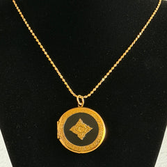 Round vintage black enamel locket with raised gold floral motif and engraved gold‑tone border on a delicate tinsel chain.