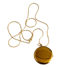 Round vintage black enamel locket with raised gold floral motif and engraved gold‑tone border on a delicate tinsel chain.