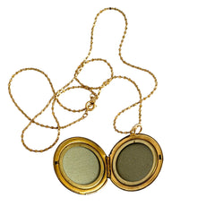 Round vintage black enamel locket with raised gold floral motif and engraved gold‑tone border on a delicate tinsel chain.