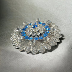 Vintage silver‑tone filigree brooch with sapphire blue and clear rhinestones in a floral design.