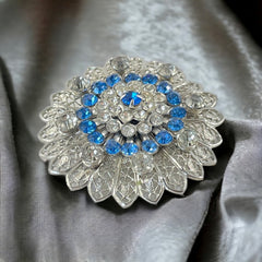 Vintage silver‑tone filigree brooch with sapphire blue and clear rhinestones in a floral design.