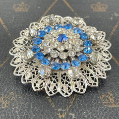 Vintage silver‑tone filigree brooch with sapphire blue and clear rhinestones in a floral design.