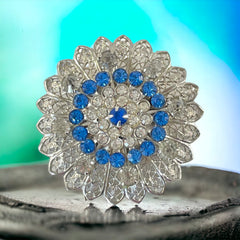 Vintage silver‑tone filigree brooch with sapphire blue and clear rhinestones in a floral design.
