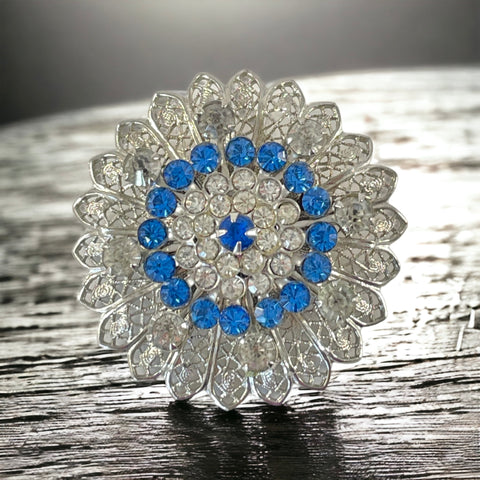 Vintage silver‑tone filigree brooch with sapphire blue and clear rhinestones in a floral design.