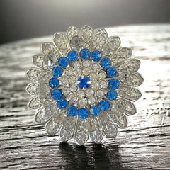 Vintage silver‑tone filigree brooch with sapphire blue and clear rhinestones in a floral design.