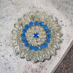 Vintage silver‑tone filigree brooch with sapphire blue and clear rhinestones in a floral design.