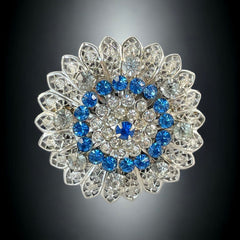 Vintage silver‑tone filigree brooch with sapphire blue and clear rhinestones in a floral design.