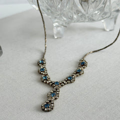 Vintage silver‑tone necklace with a delicate blue and clear rhinestone drop pendant on an adjustable chain.