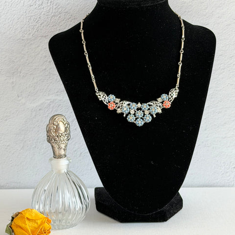 Vintage 1950s silver‑tone filigree necklace with tiny blue and coral molded flowers, clear rhinestones, and a bar‑link chain, shown from various angles.