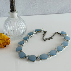Vintage 1950s necklace with baby blue moonglow teardrop thermoset panels set in silver‑tone links, displayed on a light fabric background.