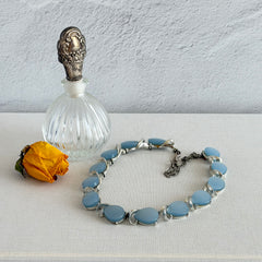 Vintage 1950s necklace with baby blue moonglow teardrop thermoset panels set in silver‑tone links, displayed on a light fabric background.