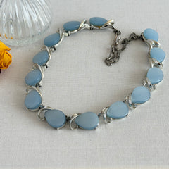 Vintage 1950s necklace with baby blue moonglow teardrop thermoset panels set in silver‑tone links, displayed on a light fabric background.