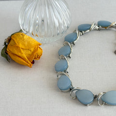 Vintage 1950s necklace with baby blue moonglow teardrop thermoset panels set in silver‑tone links, displayed on a light fabric background.