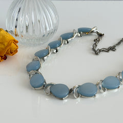 Vintage 1950s necklace with baby blue moonglow teardrop thermoset panels set in silver‑tone links, displayed on a light fabric background.