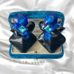 Vintage 1980s statement clip-on earrings with capri blue vitrail and black crystals in geometric cuts, set on a black leather square base.