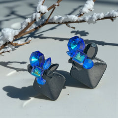 Vintage 1980s statement clip-on earrings with capri blue vitrail and black crystals in geometric cuts, set on a black leather square base.