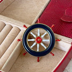 Vintage gold‑tone ship‑wheel brooch with navy, red, and white enamel, photographed on antique French script background.