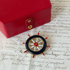 Vintage gold‑tone ship‑wheel brooch with navy, red, and white enamel, photographed on antique French script background.