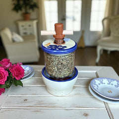 Provence ceramic herb mill with hand-painted blue lavender sprigs and green leaves on a cream base, featuring a glass chamber filled with dried herbs and a wooden crossbar handle for grinding.