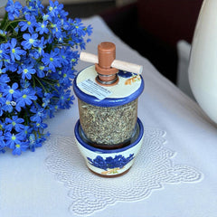 Provence ceramic herb mill with hand-painted blue lavender sprigs and green leaves on a cream base, featuring a glass chamber filled with dried herbs and a wooden crossbar handle for grinding.