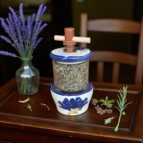 Provence ceramic herb mill with hand-painted blue lavender sprigs and green leaves on a cream base, featuring a glass chamber filled with dried herbs and a wooden crossbar handle for grinding.