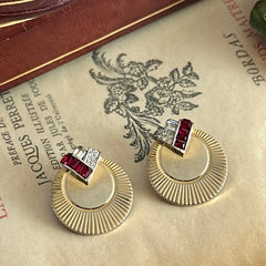 Pair of vintage Marcel Boucher gold‑tone disk clip‑on earrings with ruby‑red baguette rhinestones and clear rhinestone accents.