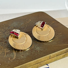Pair of vintage Marcel Boucher gold‑tone disk clip‑on earrings with ruby‑red baguette rhinestones and clear rhinestone accents.