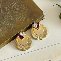 Pair of vintage Marcel Boucher gold‑tone disk clip‑on earrings with ruby‑red baguette rhinestones and clear rhinestone accents.