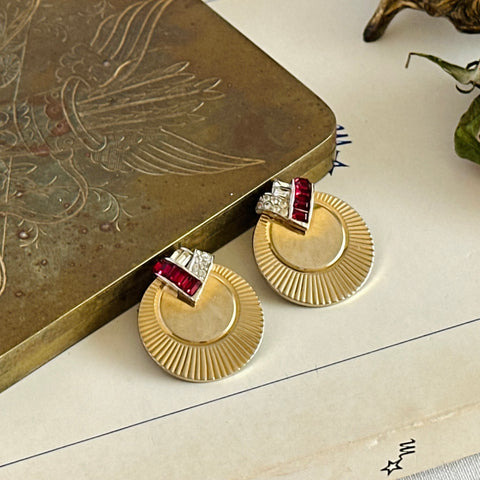 Pair of vintage Marcel Boucher gold‑tone disk clip‑on earrings with ruby‑red baguette rhinestones and clear rhinestone accents.