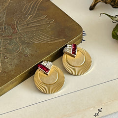 Pair of vintage Marcel Boucher gold‑tone disk clip‑on earrings with ruby‑red baguette rhinestones and clear rhinestone accents.