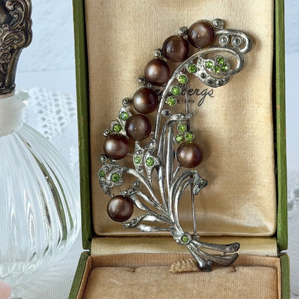 Vintage 1930s floral spray brooch with brown moonglow cabochons and green rhinestones in silver‑tone pot metal.