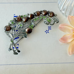 Vintage 1930s floral spray brooch with brown moonglow cabochons and green rhinestones in silver‑tone pot metal.