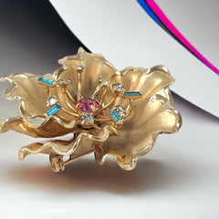 Vintage Bugbee & Niles brushed gold tone flower brooch with pink, aqua, and clear rhinestones, shown from multiple angles to highlight its dimensional petals and detailed construction.