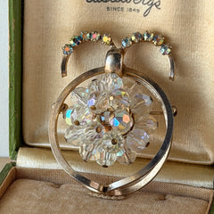 Vintage gold tone brooch featuring a cluster of iridescent aurora borealis crystals framed by curved scrolls and rhinestone accents, shown against various backgrounds.