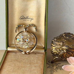 Vintage gold tone brooch featuring a cluster of iridescent aurora borealis crystals framed by curved scrolls and rhinestone accents, shown against various backgrounds.
