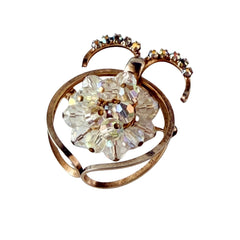 Vintage gold tone brooch featuring a cluster of iridescent aurora borealis crystals framed by curved scrolls and rhinestone accents, shown against various backgrounds.