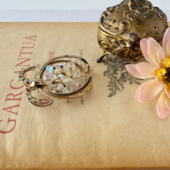 Vintage gold tone brooch featuring a cluster of iridescent aurora borealis crystals framed by curved scrolls and rhinestone accents, shown against various backgrounds.
