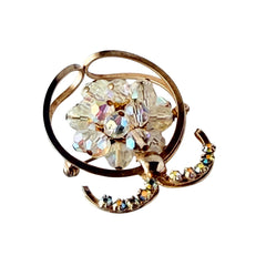 Vintage gold tone brooch featuring a cluster of iridescent aurora borealis crystals framed by curved scrolls and rhinestone accents, shown against various backgrounds.