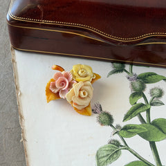 Vintage 1950s celluloid floral brooch with pink, yellow, and cream roses on a single brown leaf, shown from multiple angles.
