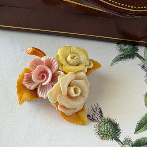 Vintage 1950s celluloid floral brooch with pink, yellow, and cream roses on a single brown leaf, shown from multiple angles.