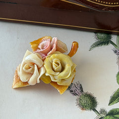 Vintage 1950s celluloid floral brooch with pink, yellow, and cream roses on a single brown leaf, shown from multiple angles.