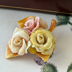Vintage 1950s celluloid floral brooch with pink, yellow, and cream roses on a single brown leaf, shown from multiple angles.