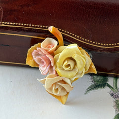 Vintage 1950s celluloid floral brooch with pink, yellow, and cream roses on a single brown leaf, shown from multiple angles.