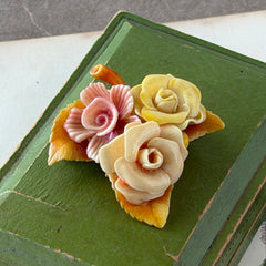 Vintage 1950s celluloid floral brooch with pink, yellow, and cream roses on a single brown leaf, shown from multiple angles.