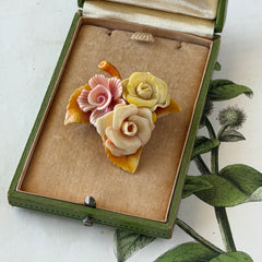 Vintage 1950s celluloid floral brooch with pink, yellow, and cream roses on a single brown leaf, shown from multiple angles.