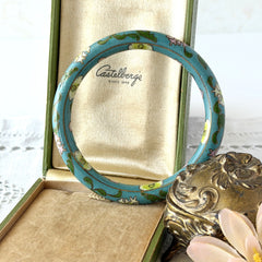 Vintage Chinese turquoise cloisonné bangle with pink and green floral enamel design photographed on linen.